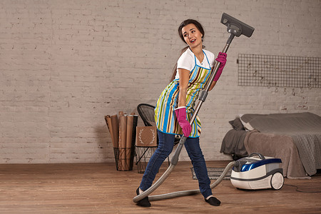 快乐的女人打扫家，用吸尘器跳舞，玩得开心，复制空间。