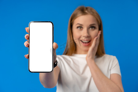 蓝色背景下的年轻女性用手指指着孤立的智能手机屏幕