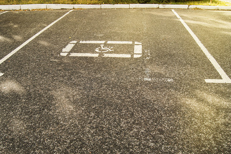 画上运输摄影照片_空荡荡的停车场的沥青上画着残疾人停车标志，阳光