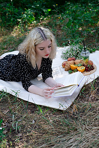 在公园里用格子布野餐的年轻女子的肖像，她正在读一本有美味小吃的书