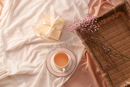 浅色织物背景托盘上的茶杯、礼盒和鲜花