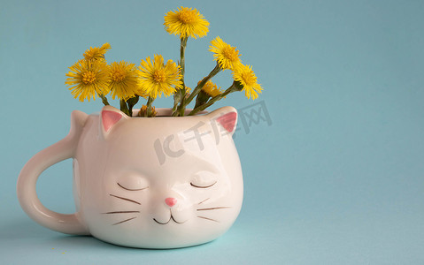 白色咖啡杯，形状为一只长着粉红色耳朵的猫，母亲和继母的花朵特写在蓝色背景上。