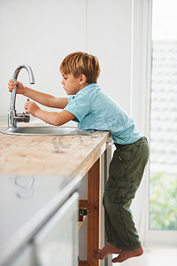 我想喝点水……一个可爱的小男孩爬上厨房柜台去水龙头。