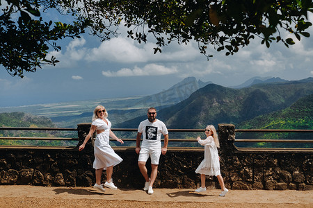 一个幸福的家庭，一个男人，一个女人和一个女儿，在毛里求斯岛的山脉和丛林的背景下快乐地跳跃。毛里求斯岛丛林中的一对夫妇和女儿穿着白色的衣服在非洲行走，