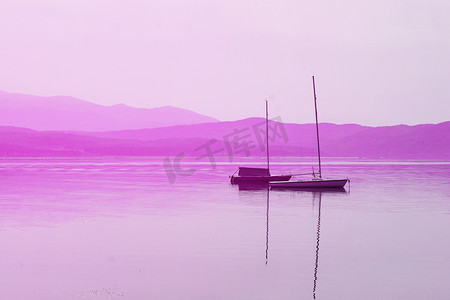 在粉红色调的群山背景下，水面上有桅杆的船