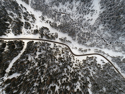 小汽车俯视图摄影照片_白雪皑皑的阿尔卑斯山上弯曲道路的俯视图