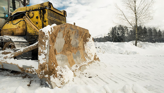 带铲斗的黄色履带式拖拉机推土机在冬季清理道路上的积雪。