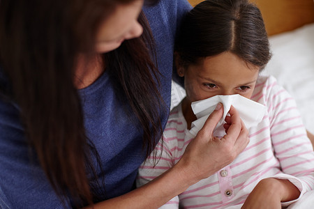 当感冒袭来时……一位母亲帮助她生病的女儿擤鼻涕的镜头。