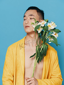 韩国一束花摄影照片_身穿黄色外套、蓝色背景上有一束白花的可爱韩国男人