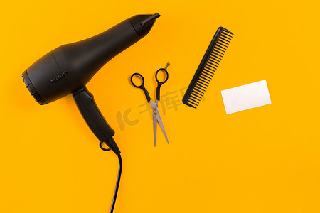 黄纸背景上的黑色吹风机、梳子和剪刀。
