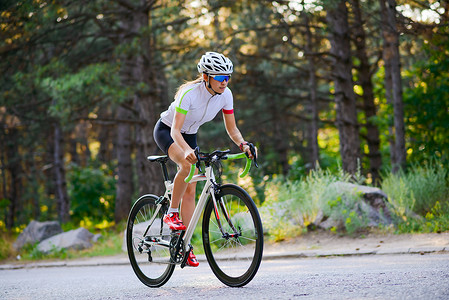 炎热摄影照片_炎热的夏日，年轻女子自行车手在森林的自由道路上骑公路自行车。