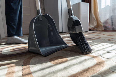 簸箕摄影照片_清洁。用扫帚把地板上的垃圾打扫干净。用刷子把灰尘和污垢扫到簸箕里。在家里用扫帚扫地毯。室内清洁工具。