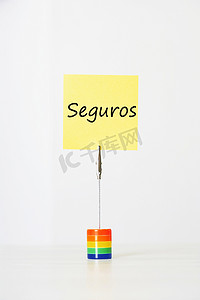 粘性的摄影照片_带有西班牙语文字“seguros”（保险）的粘性信纸夹在彩色卡夹上