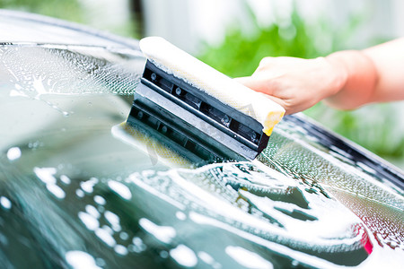 新店开业洗车摄影照片_男人在洗车时清洁挡风玻璃