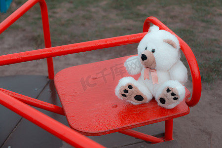 特写一只泰迪熊正坐在红色的儿童秋千上。