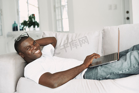 一个快乐的非洲人长相躺在沙发上，手里拿着笔记本电脑