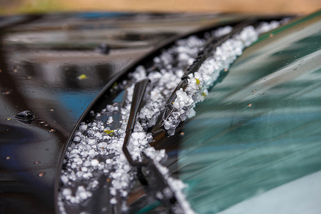 夏季暴风雨过后，黑色汽车引擎盖上的小冰雹冰球