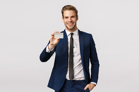 英俊、幸运的成功商人穿着经典西装，用信用卡支付，拿着银行卡显示它，微笑着高兴，进入机场休息区，站在白色背景