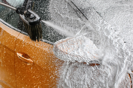 在洗车时，黄色汽车侧镜的细节覆盖着厚厚的白色洗发水泡沫，喷洒更多。