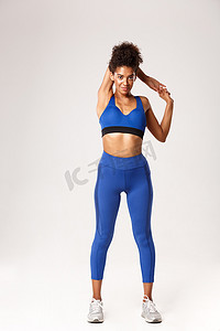 全长微笑迷人的非洲裔美国健身女孩穿着蓝色运动服，伸展双手，锻炼前热身，站在白色背景下