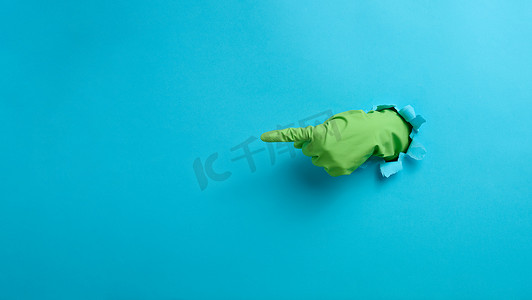 一只戴着绿色乳胶手套的手将手指指向蓝色背景。