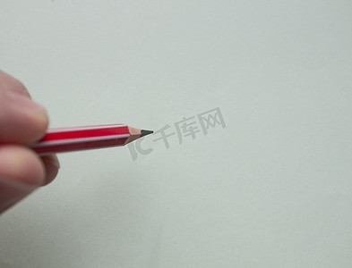 握铅笔摄影照片_一名男子用手指在浅色纸上握着一支红色铅笔。