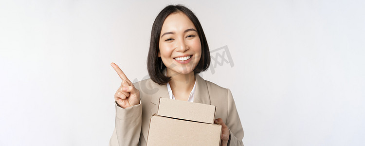 微笑的亚洲女售货员用手指指着复印空间，拿着带送货单的盒子，站在白色背景上