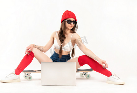 戴着红帽和红袜子的女孩坐在长板上，白色背景上有一台笔记本电脑