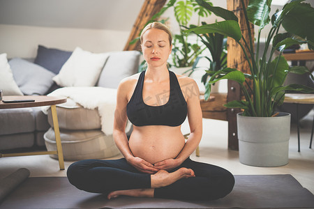 训练瑜伽的年轻美丽的孕妇，爱抚她的腹部。