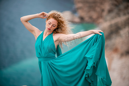 飘逸的长裙摄影照片_身着翡翠裙的女子，长着丝绸长翅膀的时装模特，飘逸的长裙，飞舞的布料在堤岸上。