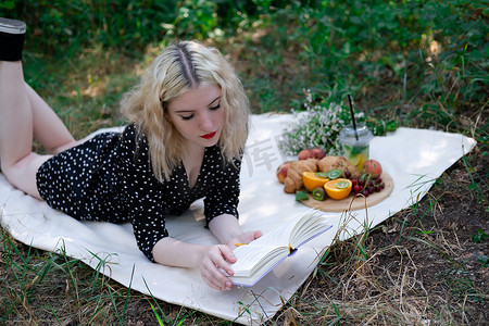 绿色格子布摄影照片_在公园里用格子布野餐的年轻女子的肖像，她正在读一本有美味小吃的书