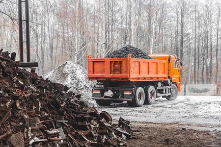 冬天，工业区或建筑工地的自卸车从车身上卸焦煤，旁边是一堆金属废料和垃圾