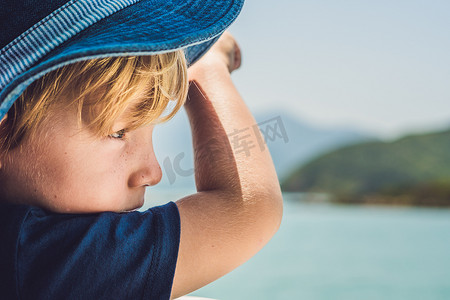 可爱的游艇摄影照片_阳光明媚的日子里，可爱的男孩从游艇板上望向蓝色的大海