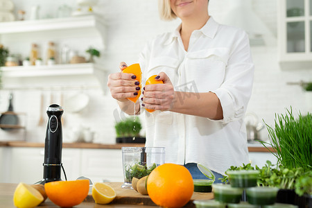 一位女士的手挤橙汁制作小麦汁冰沙的特写。