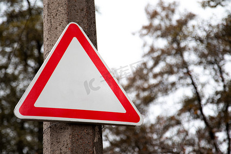空的红色三角形路标，街道上没有文字和标志，背景是绿树。