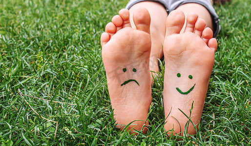 年底banner摄影照片_有油漆图案的婴儿脚在绿色的草地上微笑和悲伤。