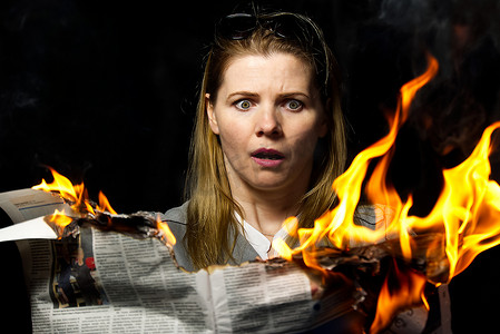 燃烧报纸摄影照片_一名妇女拿着一份燃烧的报纸。