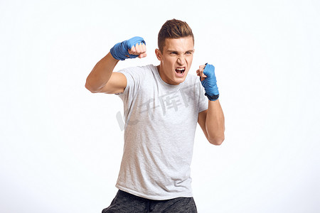 活动浅色背景摄影照片_戴着蓝色手套的运动型男拳击手在浅色背景裁剪视图中练习拳击