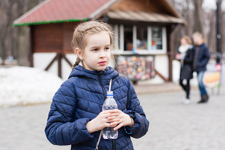 在城市公园的一辆食品卡车的背景下，可爱的女孩拿着一瓶饮用水。
