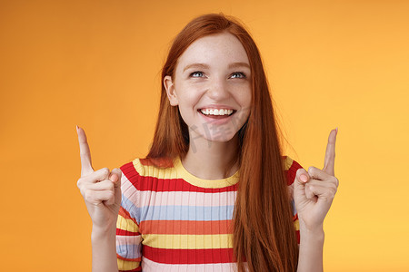 快乐开朗的红发女孩在游乐园里玩得开心，高兴地笑着指着食指向上享受娱乐，站在橙色背景下开心地笑着