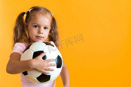 经典黑白摄影照片_带着经典黑白足球的正宗可爱微笑学龄前小女孩看着黄色背景的相机。