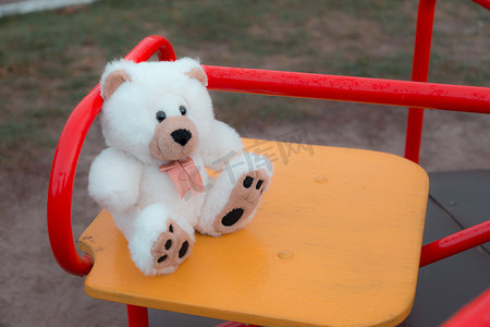 特写一只泰迪熊正坐在红色的儿童秋千上。