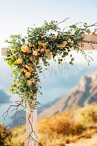 以玫瑰和绿色树枝装饰的婚礼拱门的一角，以群山为背景