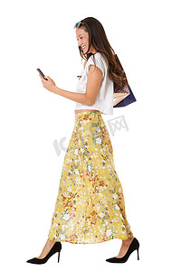 白色连衣裙摄影照片_在孤立的白色背景下，带着手机和购物袋走路的微笑亚洲女性的侧面肖像