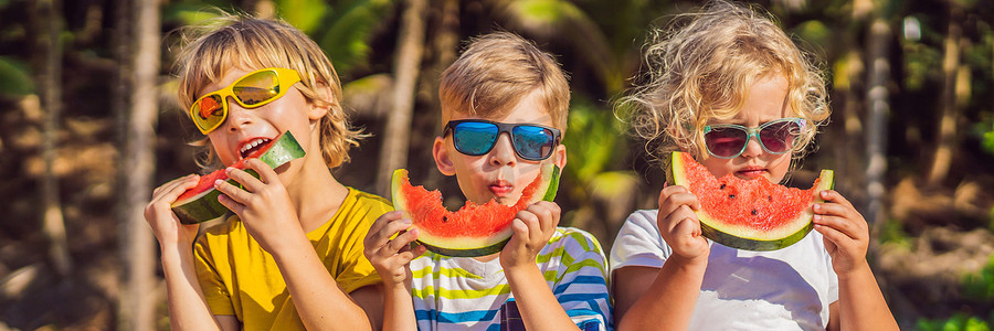 西瓜大海摄影照片_孩子们戴着太阳镜在沙滩上吃西瓜横幅，长版