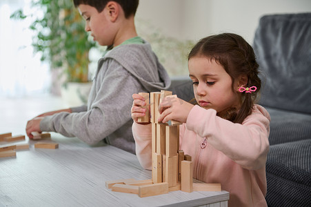 有创造力的孩子，欧洲男孩和女孩玩游戏，在高层建筑结构中堆叠木制玩具块。