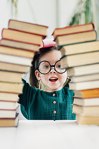 学龄前小女孩戴着圆形眼镜，身穿绿色连衣裙，身后是书拱门。