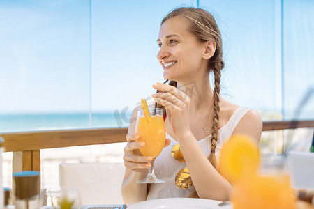 喝酒的美女摄影照片_度假中的美女在海滩餐厅享用橙汁