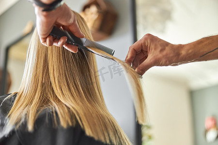 剪头发摄影照片_理发师正在为金发女人剪头发是沙龙