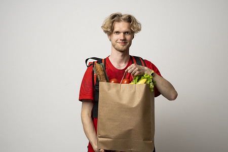 男人拿着纸袋，里面装着白色背景的杂货店的新鲜产品。